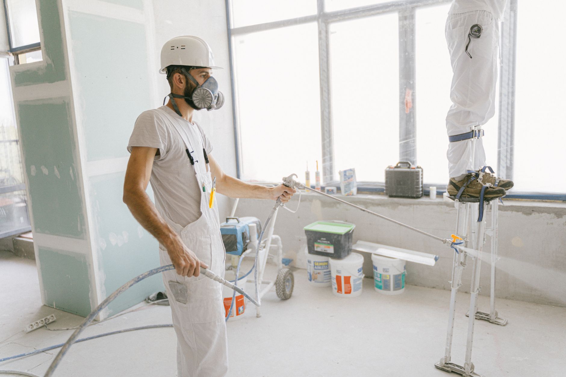 Two construction workers wearing protective gear and painting interior walls for a renovation project in Pasadena, CA